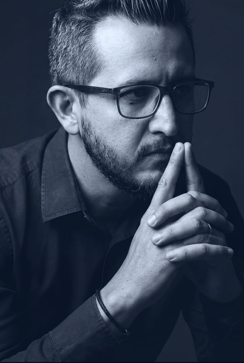 Retrato profissional de André Alves em tom azul escuro, pensativo, com as mãos entrelaçadas